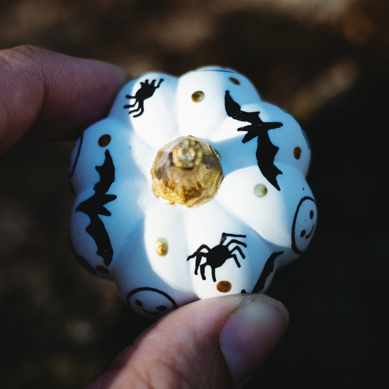 Decorative hand painted white pumpkin with black spider and bat designs held by a hand against a dark background