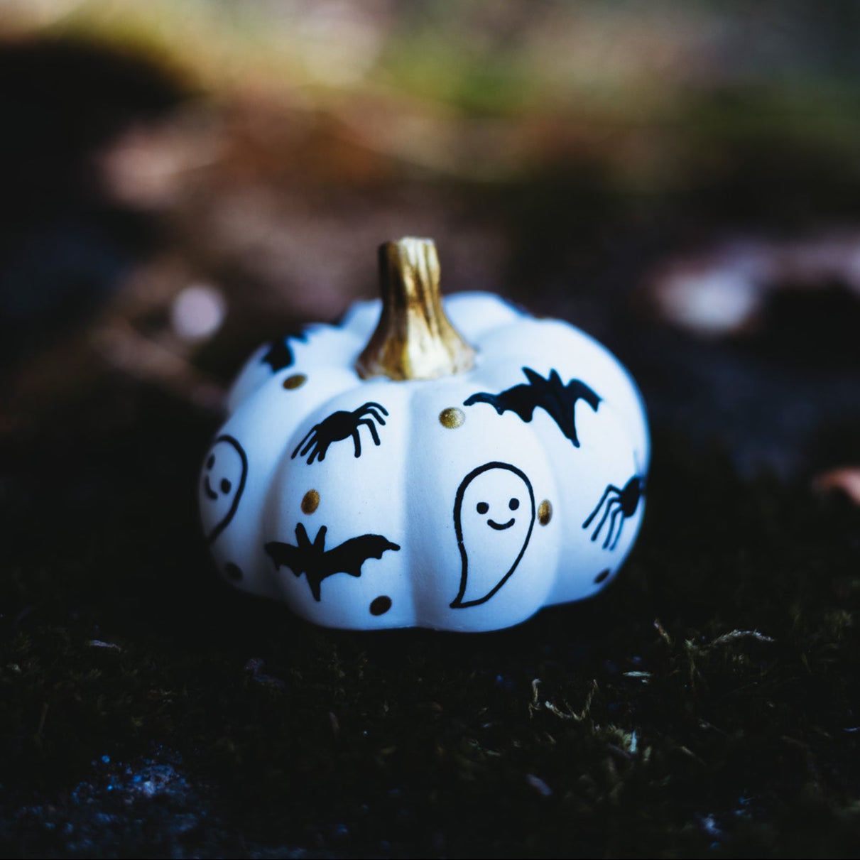 Small white decorative pumpkin with black  ghost, bat, and spider decorations on a dark background