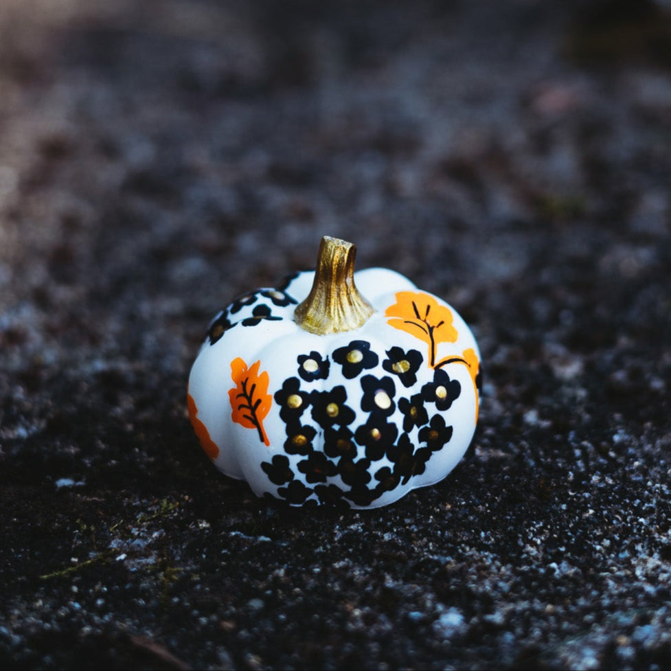 Small decorative pumpkin with black and orange patterns on a dark, textured surface.
