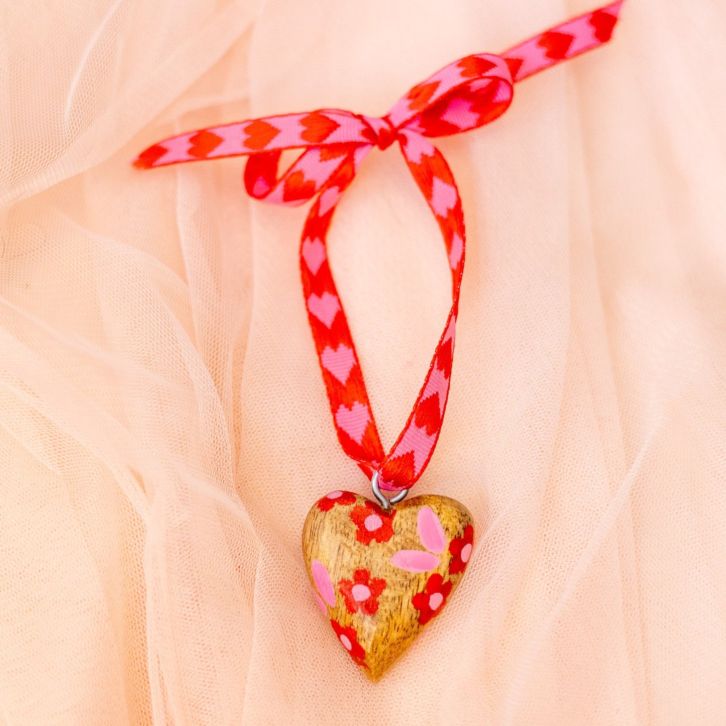 Heart-shaped pendant with floral design on a red and white checkered ribbon against a soft pink background