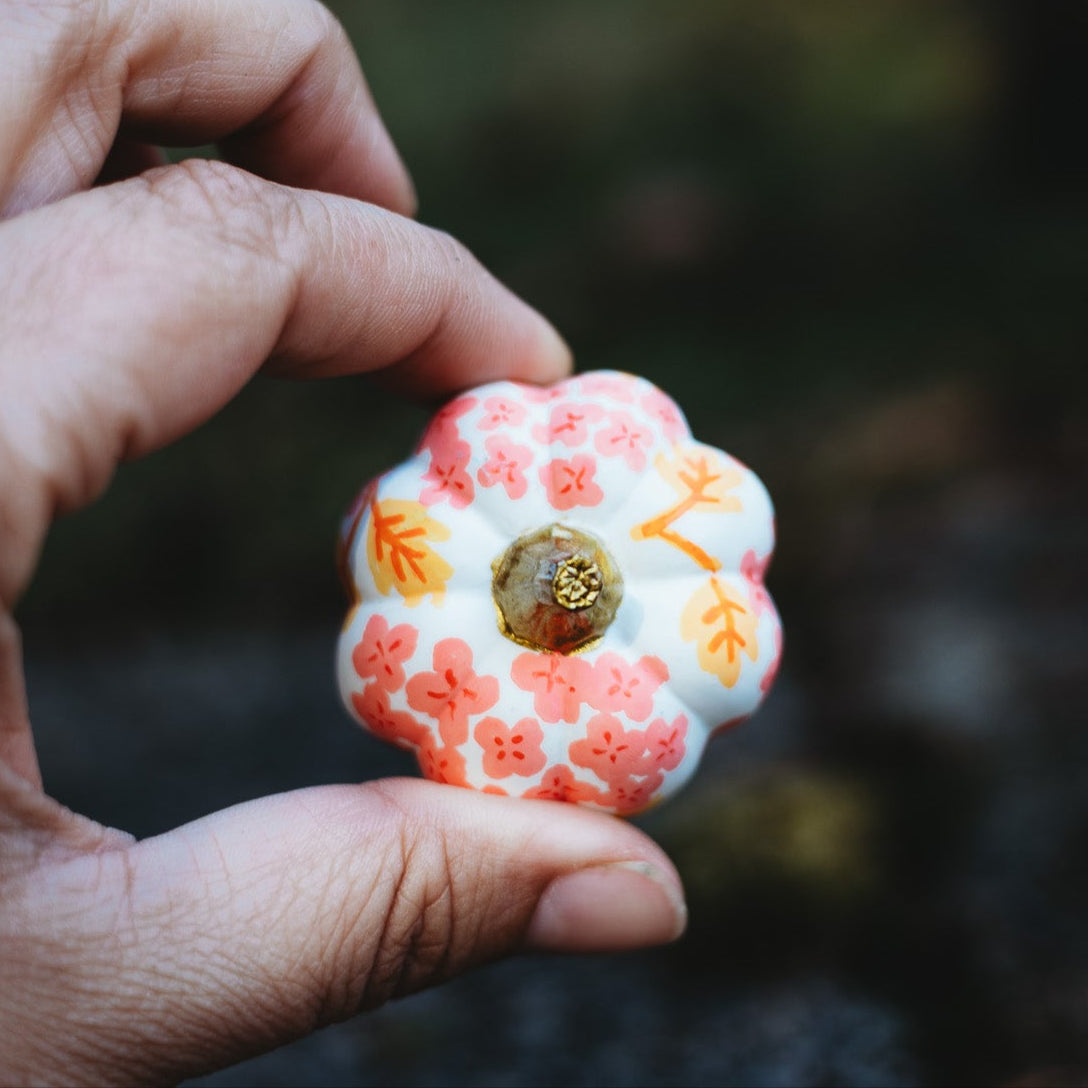 Hand holding a decorative item with floral design against a blurred natural background