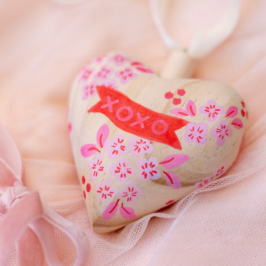 Heart-shaped object with floral patterns and 'XOXO' text on a soft pink background