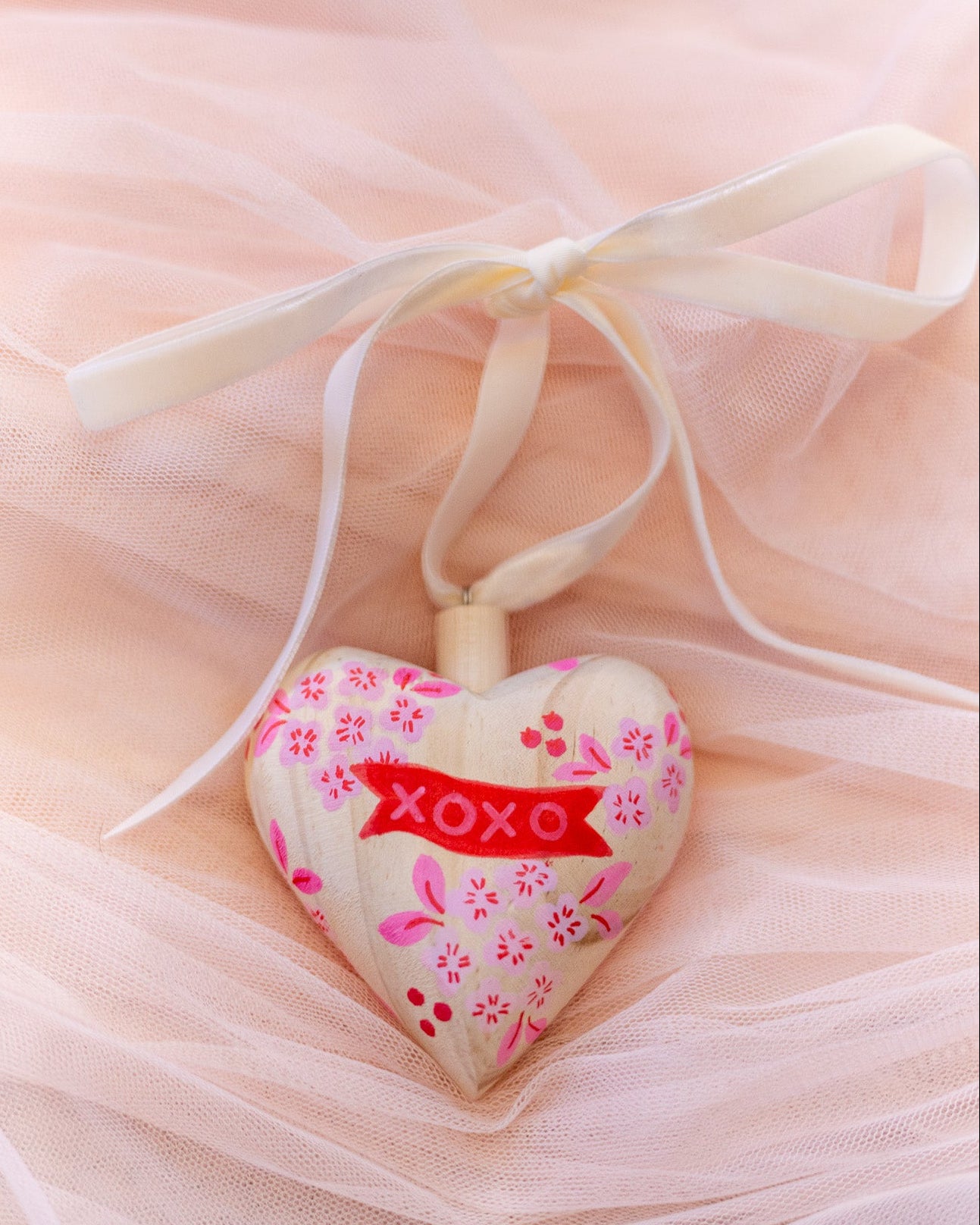 Heart-shaped decorative item with 'XOXO' on a soft pink background