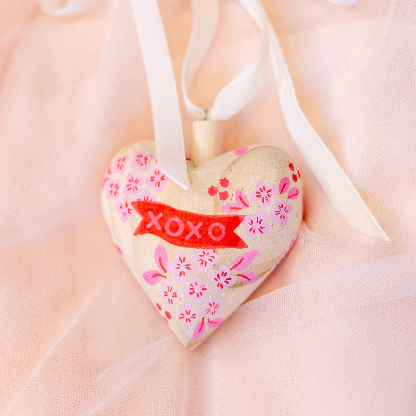 Heart-shaped ornament with 'XOXO' on a soft pink background