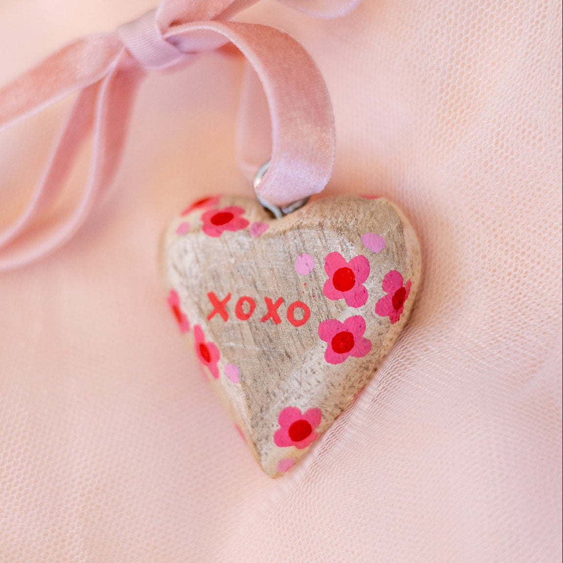 Heart-shaped decorative item with 'XOXO' and floral patterns on a pink background