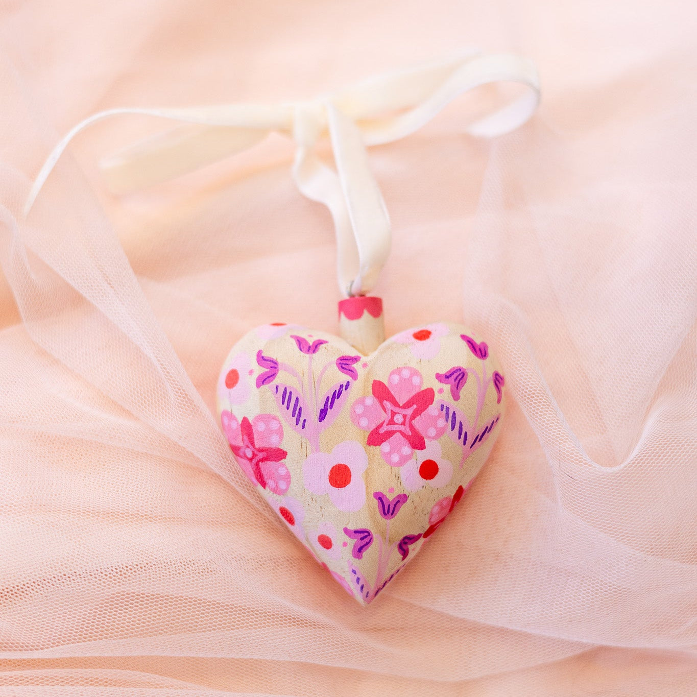 Heart-shaped fabric ornament with floral patterns on a soft pink background