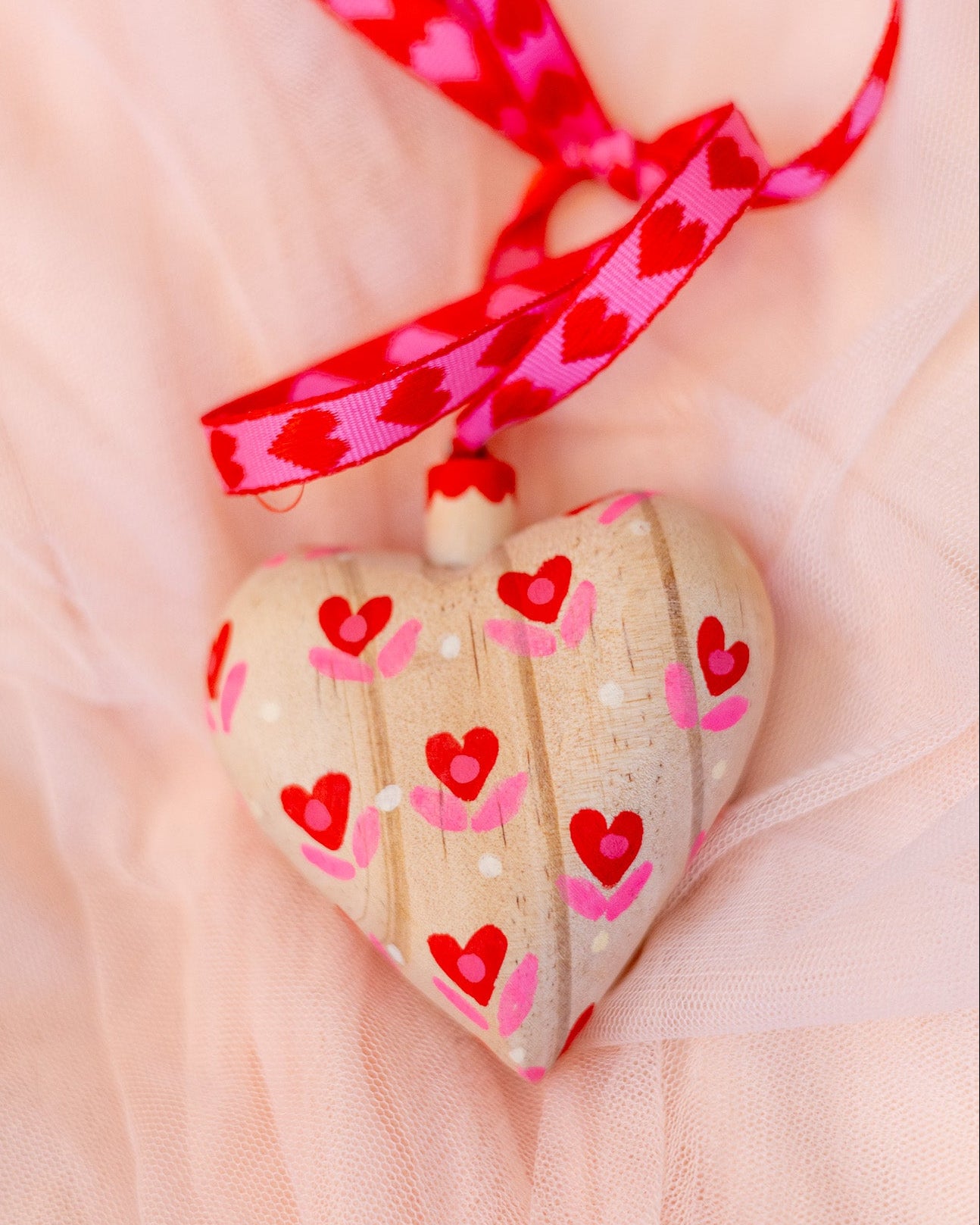 Heart-shaped wooden ornament with red and pink heart patterns on a pink fabric background