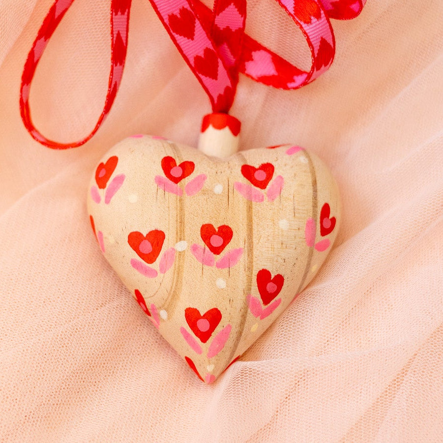 Heart-shaped ornament with red hearts and a red ribbon on a soft pink background