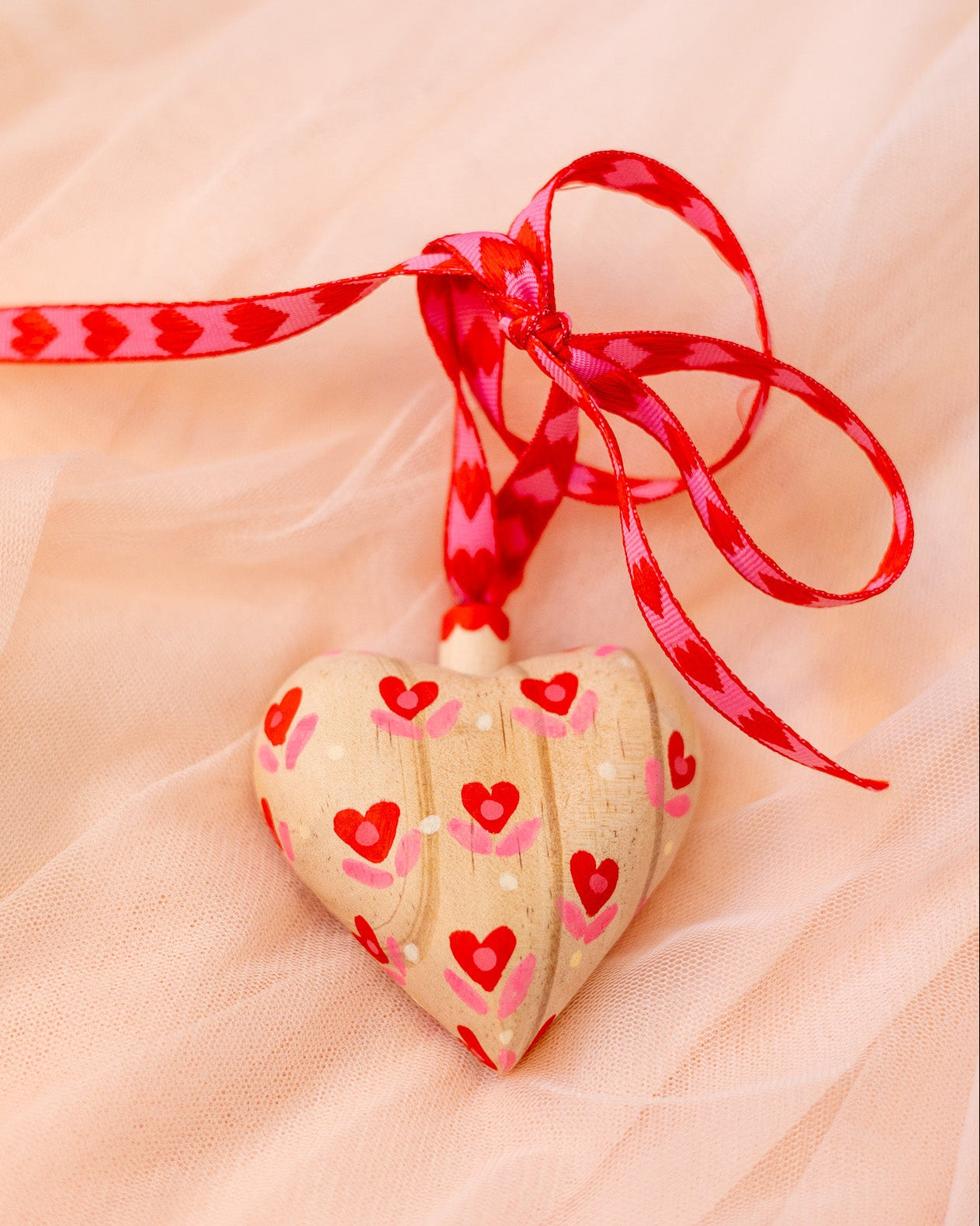 Heart-shaped cookies with red heart decorations on a pink ribbon against a soft pink background