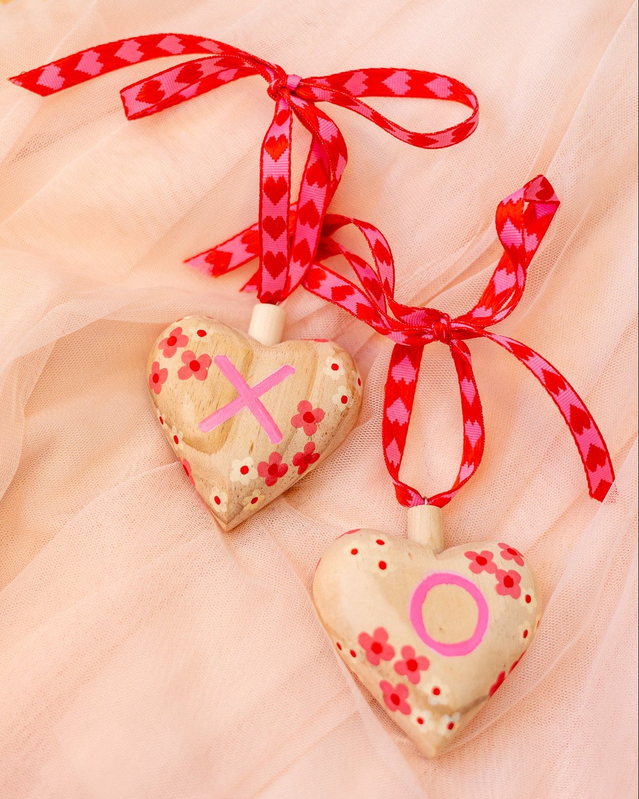 Heart-shaped wood ornaments with 'X' and 'O' on a pink background