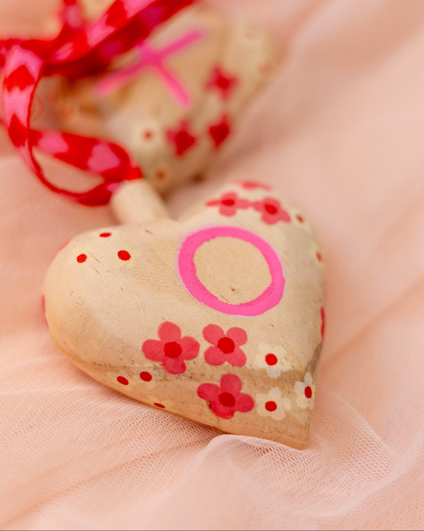 Heart-shaped wooden ornament with pink decorations on a soft pink background