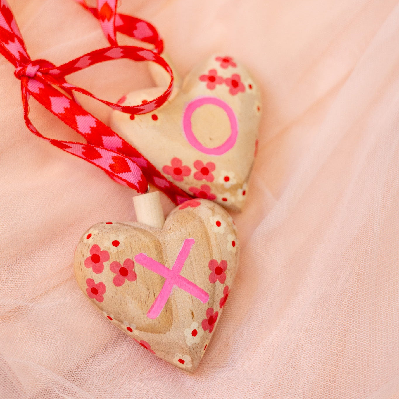 Heart-shaped wooden ornament with pink decorations on a soft pink background