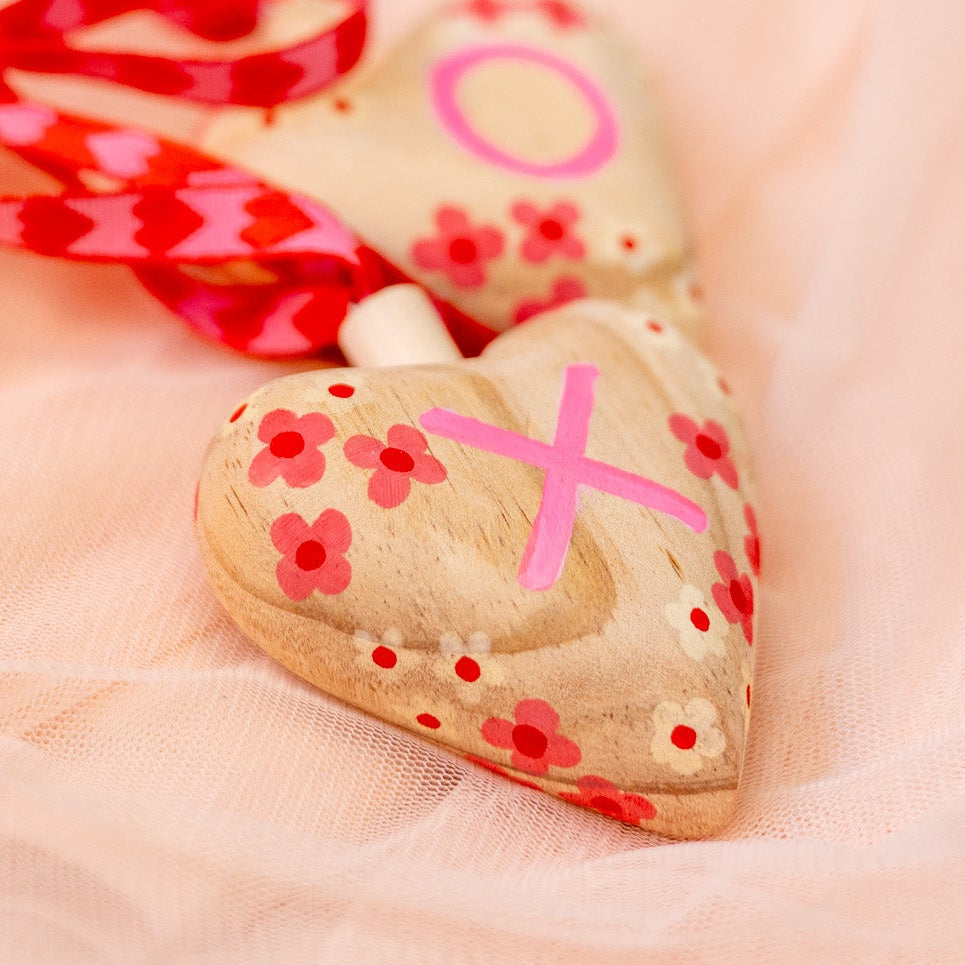 Heart-shaped wooden ornament with pink decorations on a soft pink background