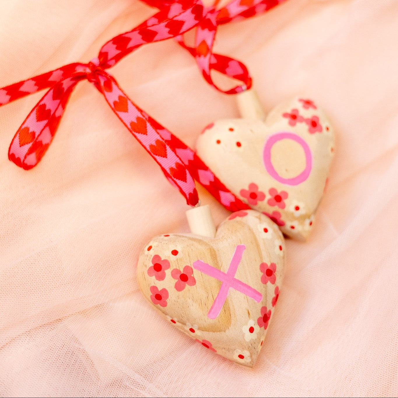 Heart-shaped wooden ornament with pink decorations on a soft pink background