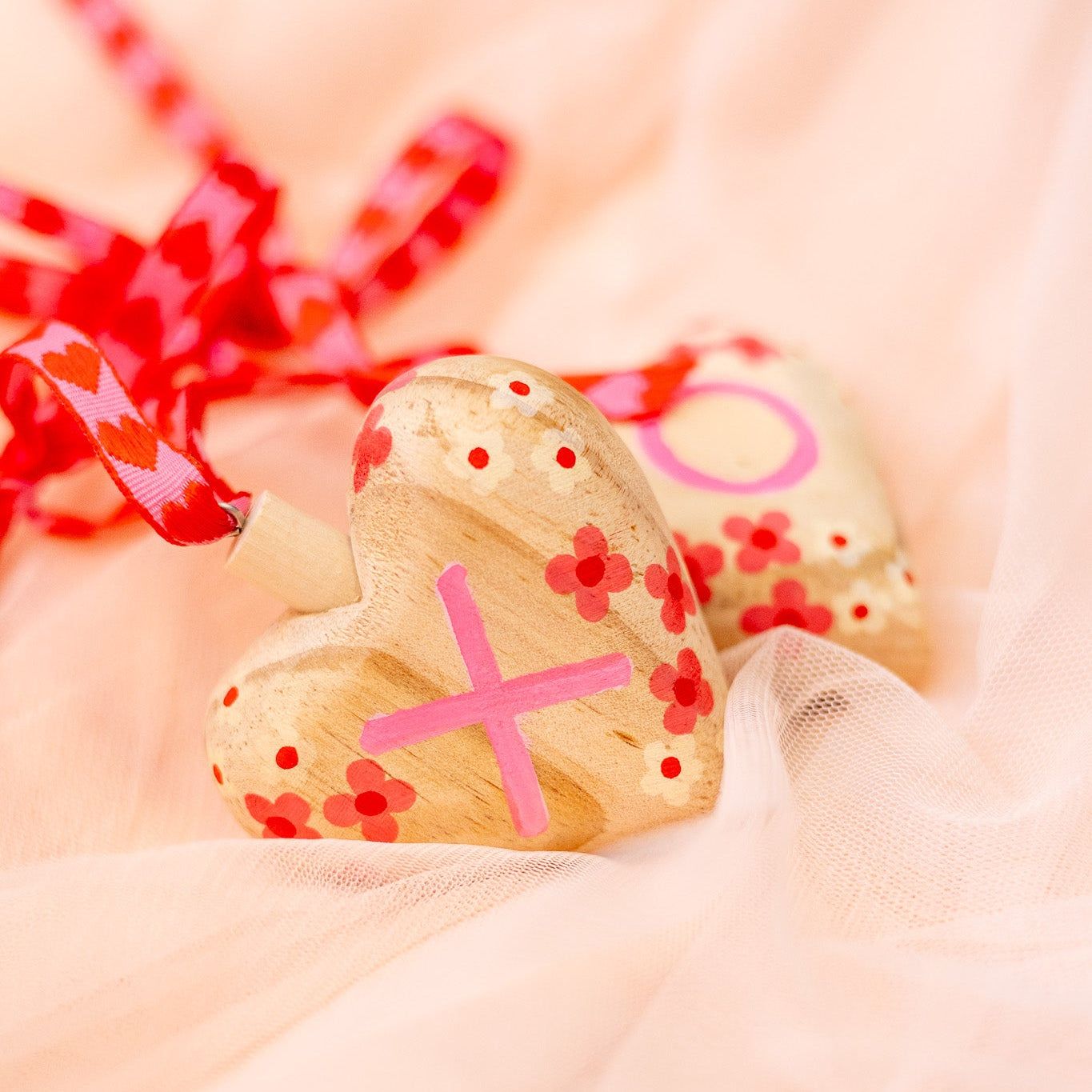 Heart-shaped wooden ornament with pink decorations on a soft pink background