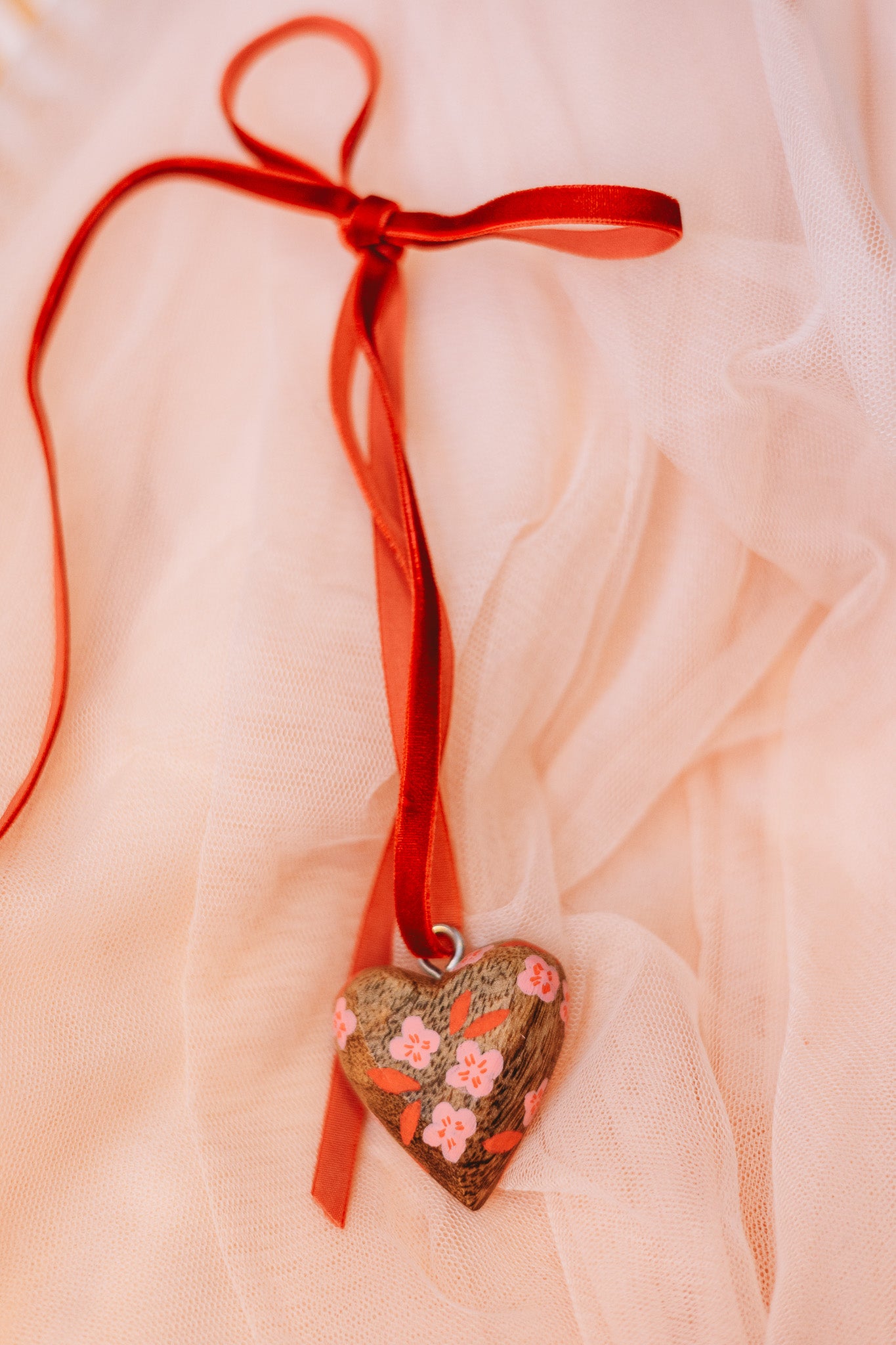 Heart-shaped decorative item with floral patterns and a red ribbon on a soft pink fabric background