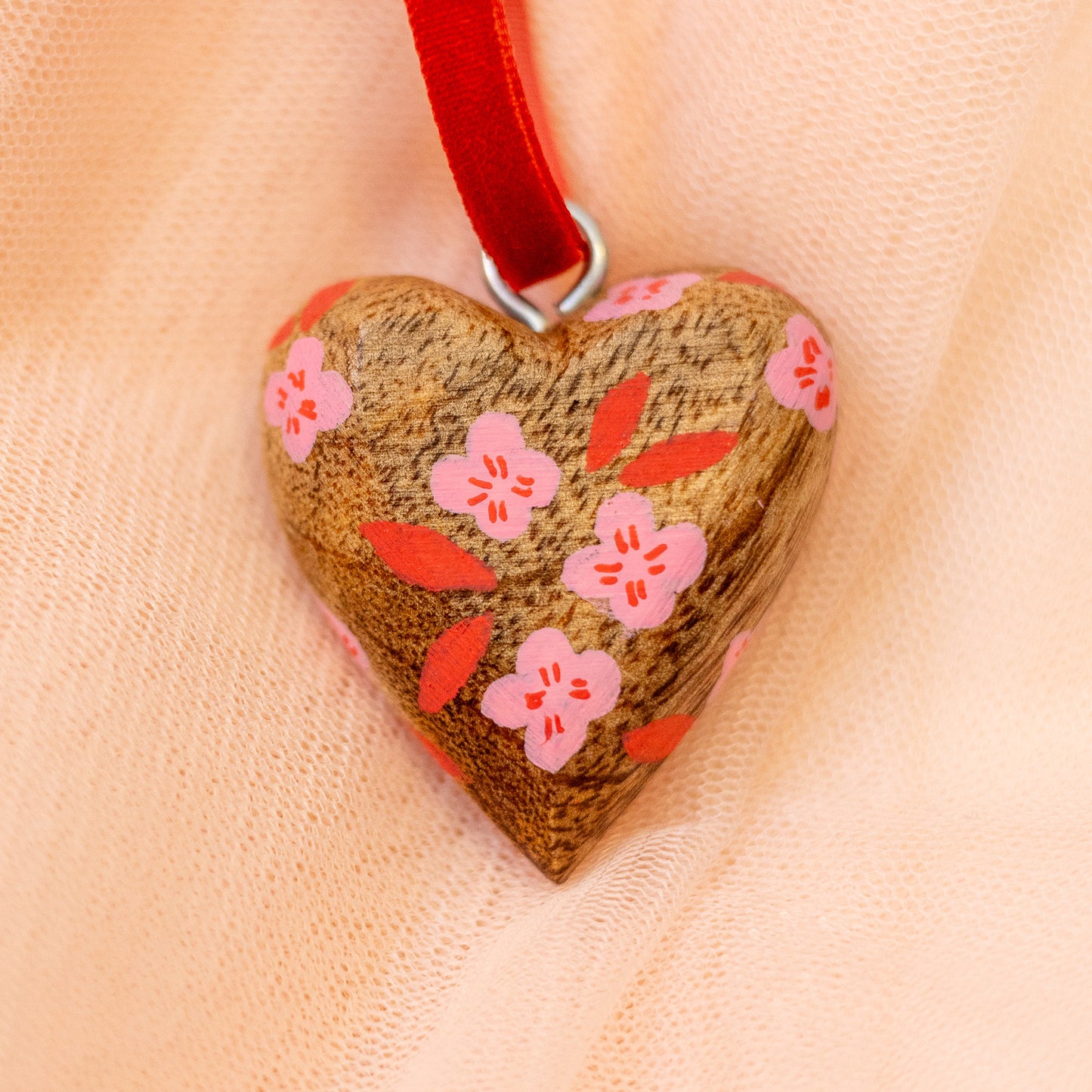 Heart-shaped pendant with floral design on a red ribbon against a beige background