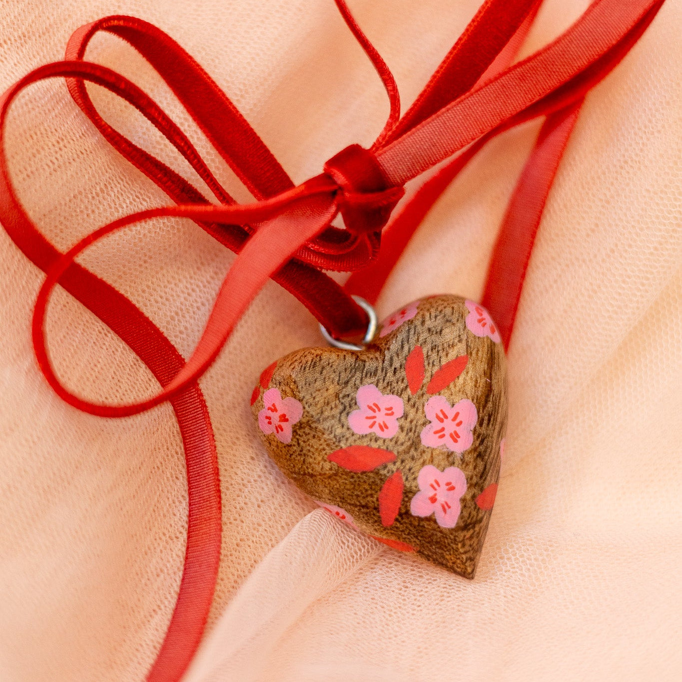 Heart-shaped pendant with floral design on a red ribbon against a beige background