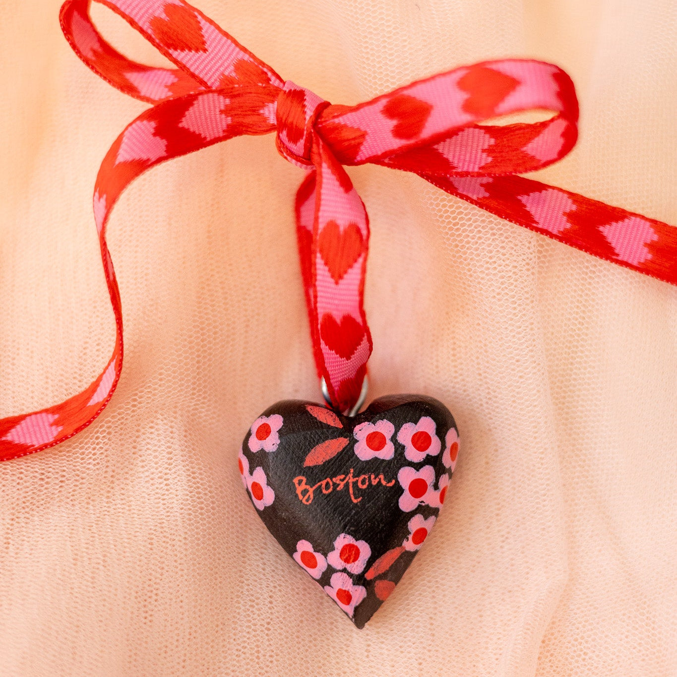 Heart-shaped pendant with floral design and red ribbon on sheer fabric