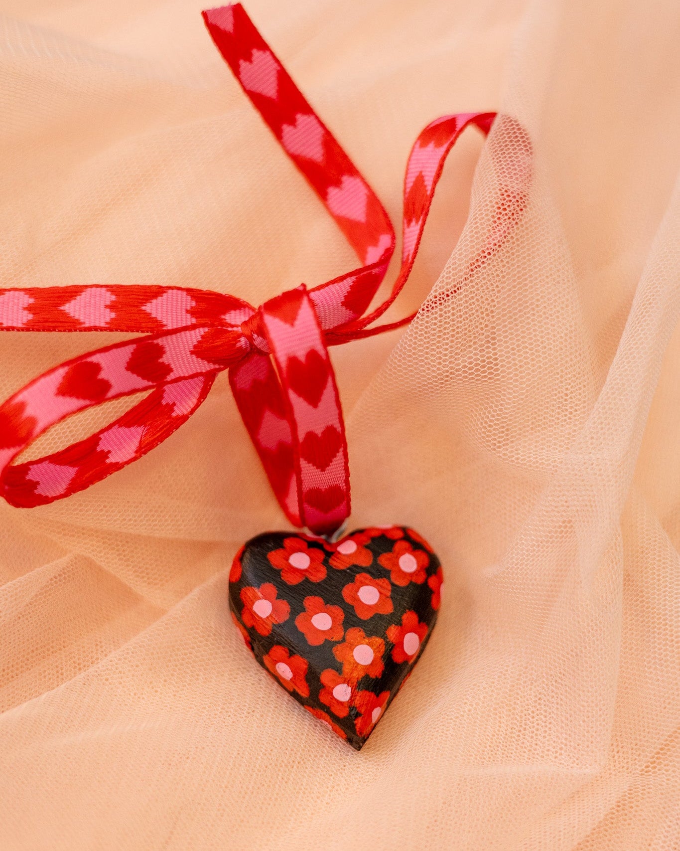 Heart-shaped ornament with floral pattern and red ribbon on a sheer fabric background