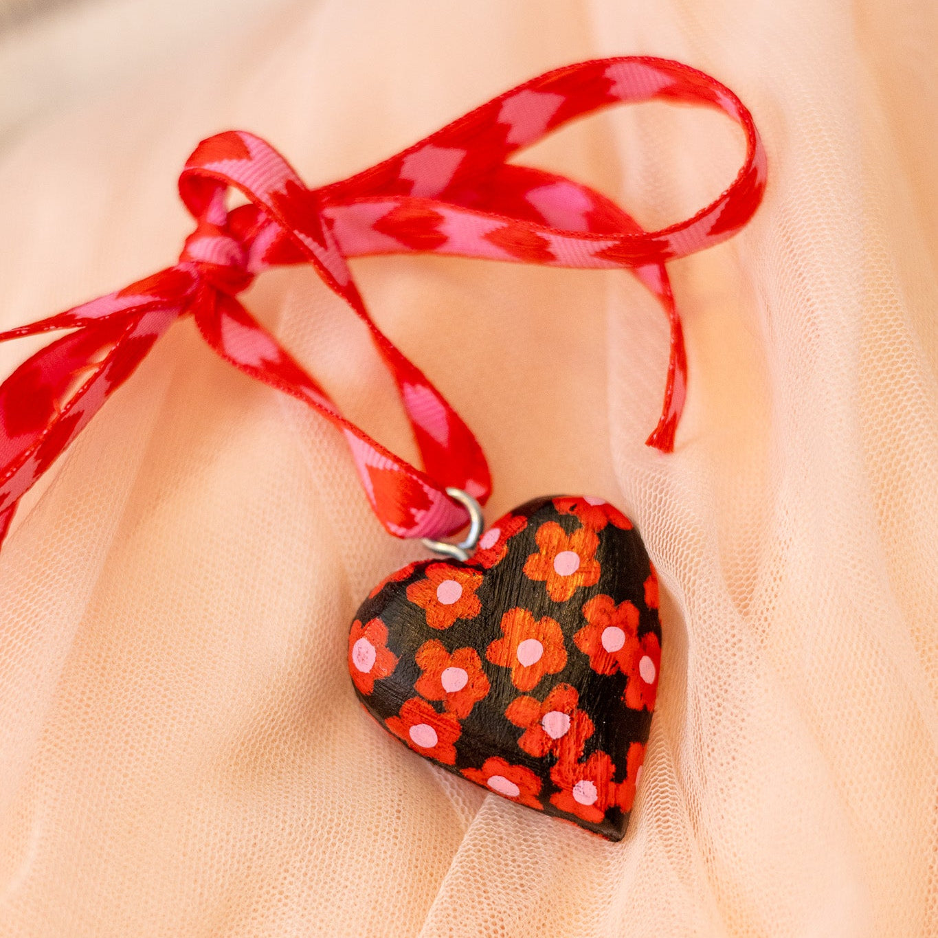 Heart-shaped pendant with floral design and red ribbon on a light fabric background