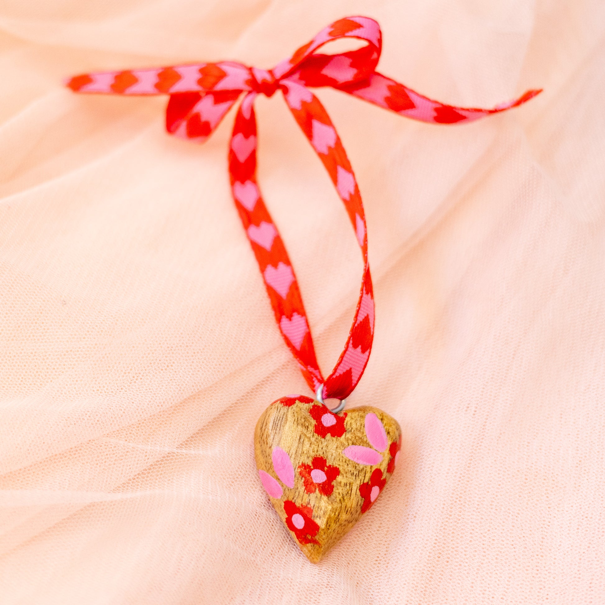 Heart-shaped ornament with floral design and red ribbon on a soft pink background