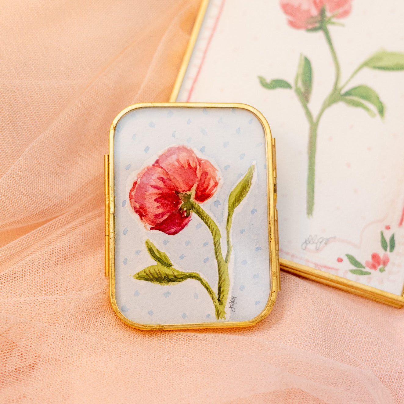 Decorative gold frame with a pink peony flower painting and a red ribbon on a sheer fabric background