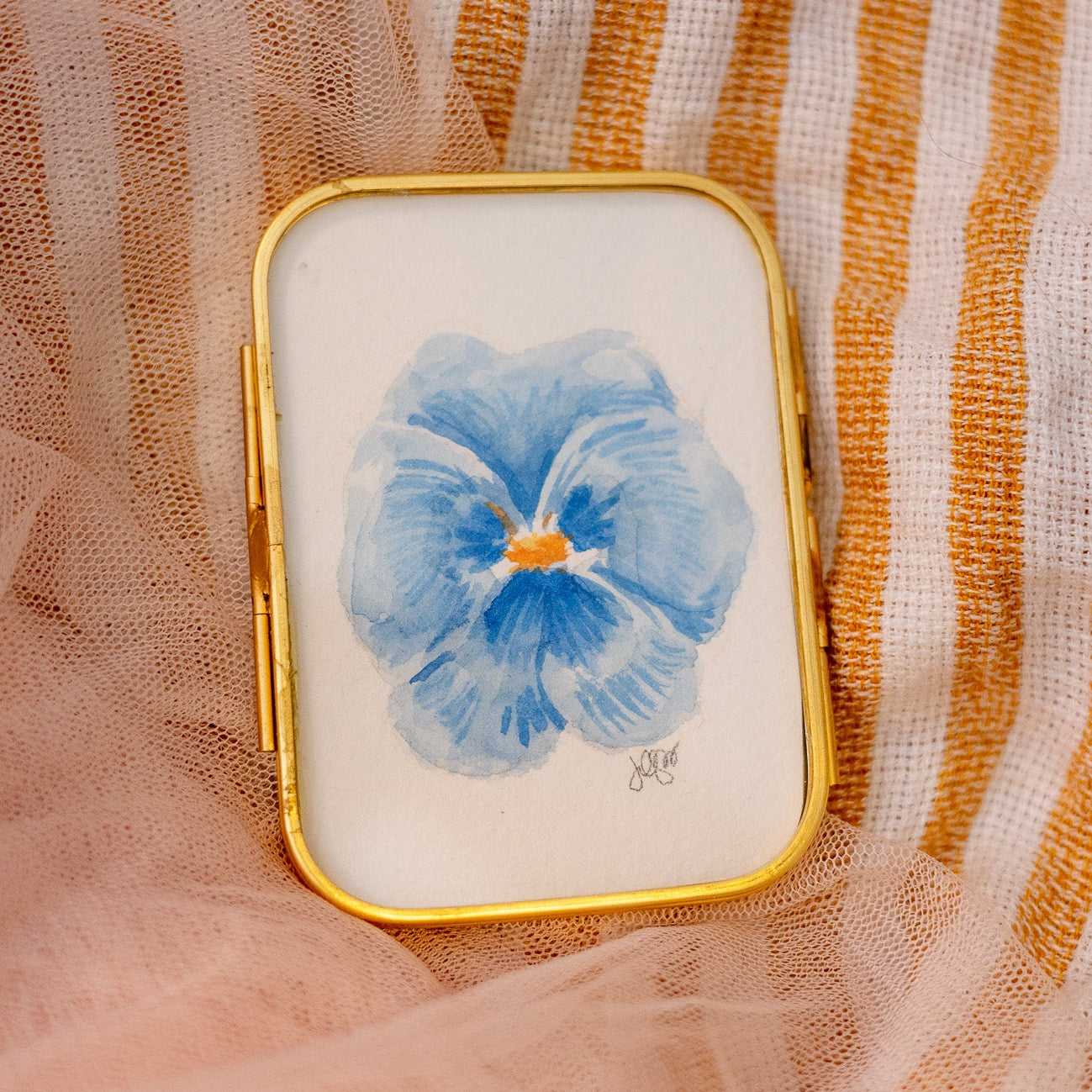 Small rectangular gold frame with a blue pansy flower painting  on a textured fabric background