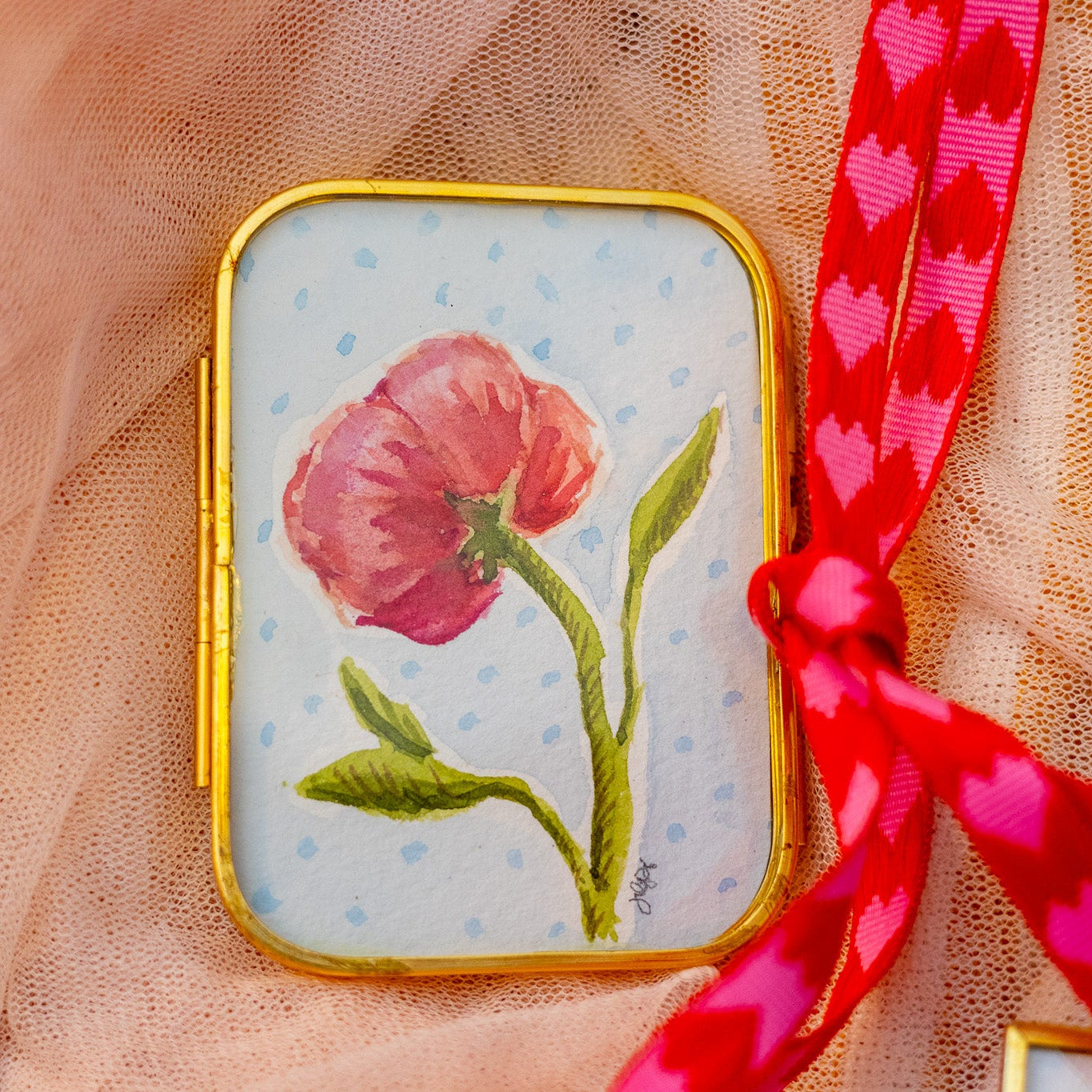 Decorative gold frame with a pink peony flower painting and a red ribbon on a sheer fabric background